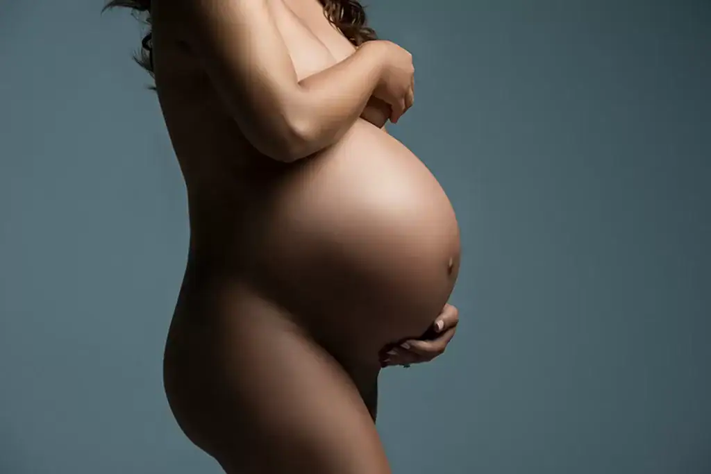 Elegant nude maternity portrait of a pregnant woman in side profile, gently holding her belly to highlight the beauty of motherhood and feminine strength