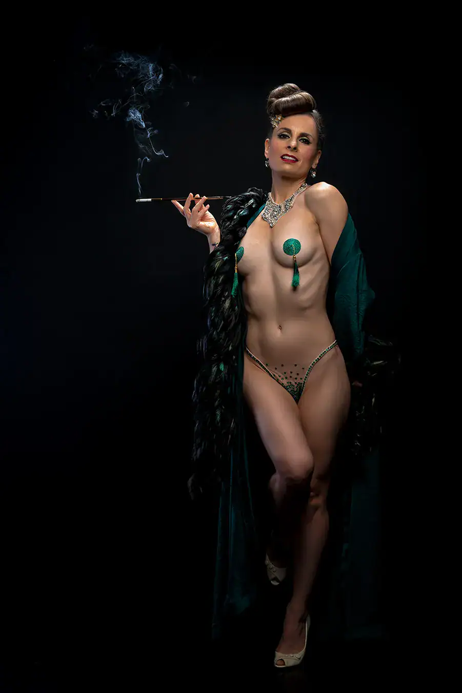 Elegant Burlesque Glamour in Emerald and Feathers Confident woman in emerald burlesque lingerie and feathered robe, holding a vintage cigarette holder with rising smoke against a dark background