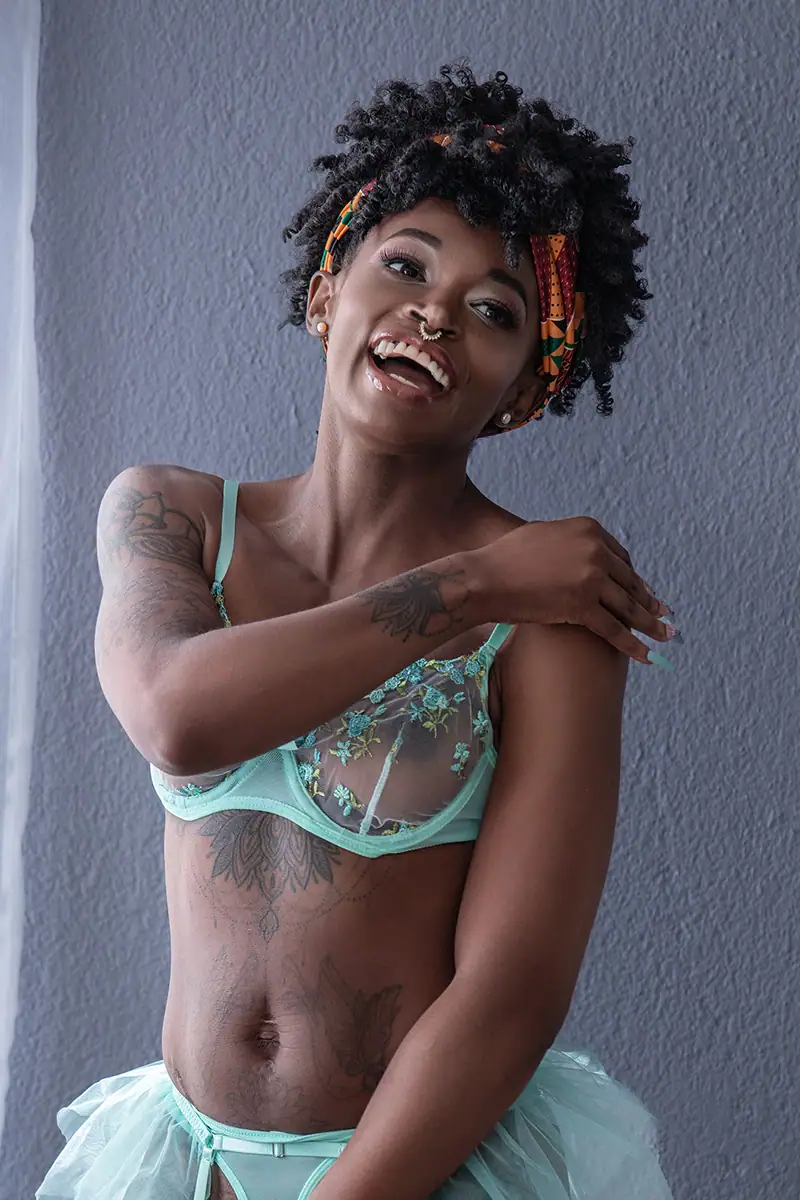 A sensual and artistic nude portrait of a woman with white handprint body paint applied to her breasts and hands, captured against a black backdrop. Her striking pose and confident gaze emphasize her beauty and the boldness of the body art.