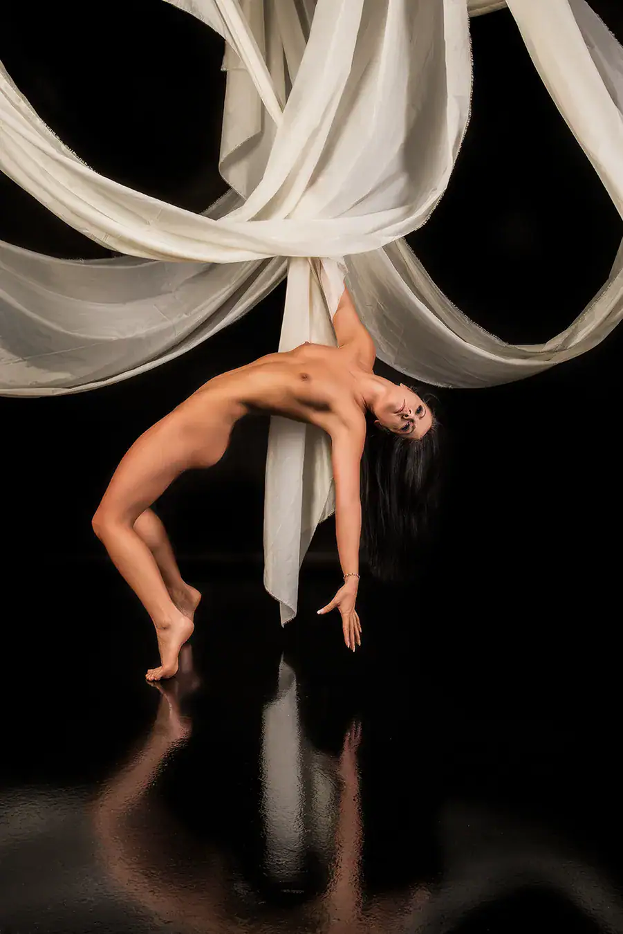 Aerial Silk Conceptual Fine Art Nude Fine art nude model suspended upside down among flowing white aerial silks against a black background
