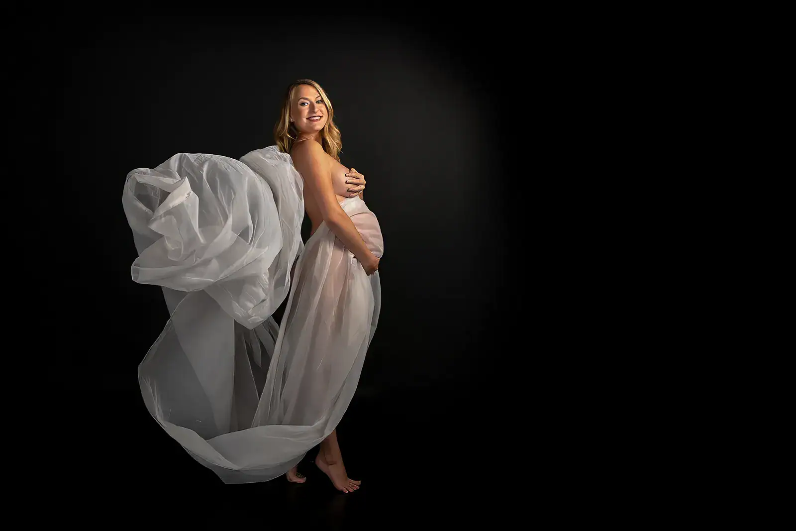 Fine Art Maternity Portrait with Flowing Fabric Pregnant woman surrounded by flowing white fabric in a dramatic fine art maternity portrait
