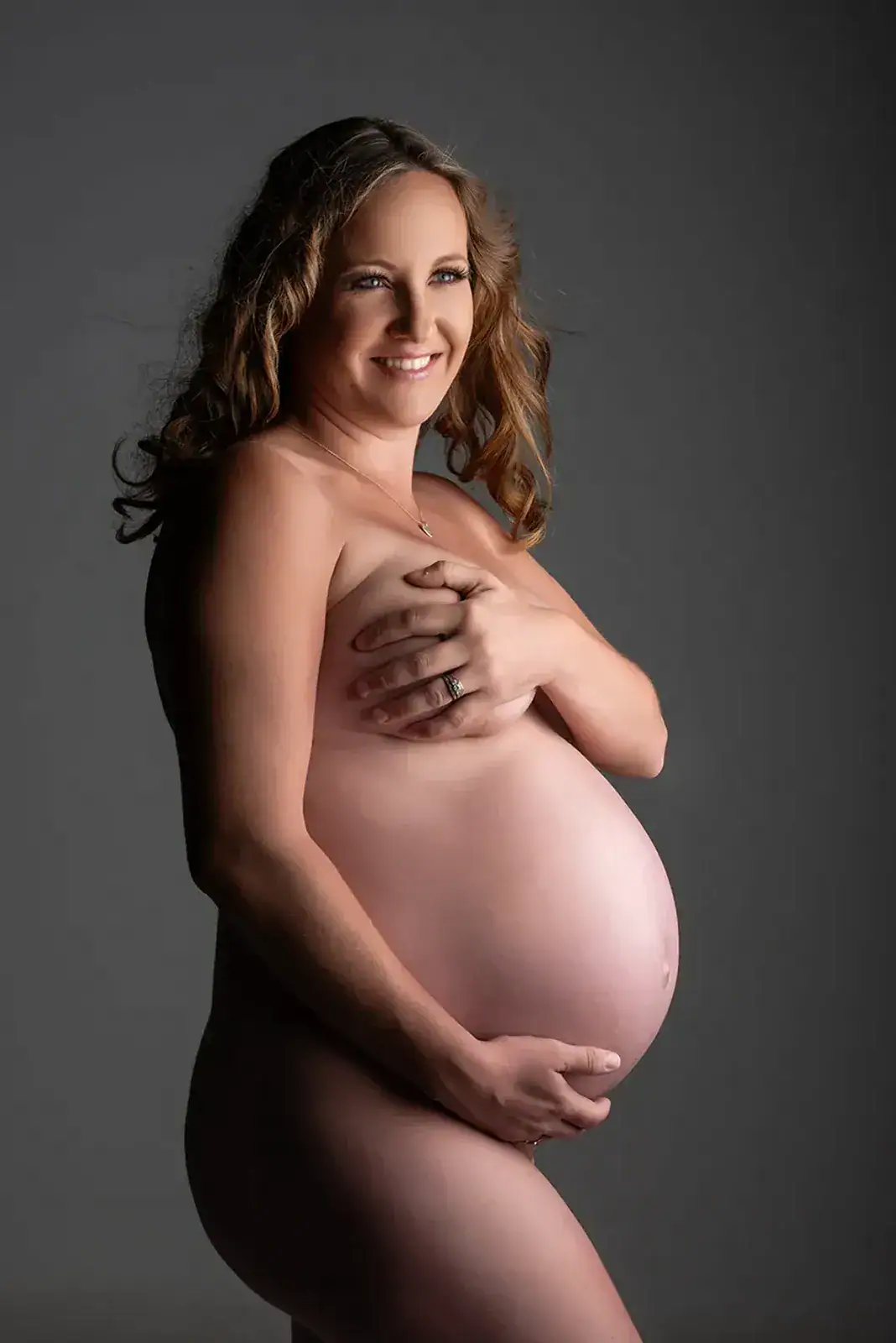 Natural Nude Maternity Portrait Pregnant woman photographed in a tasteful nude maternity portrait against a softly lit studio background
