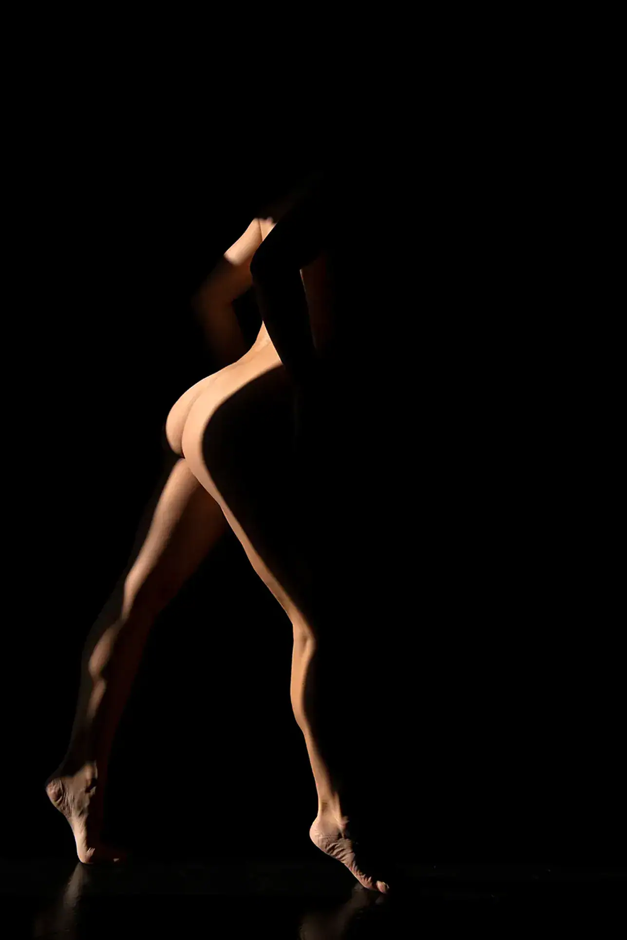 Sculptural Shadow Artistic Nude Female figure emerging from darkness with narrow dramatic lighting defining the shape of her body