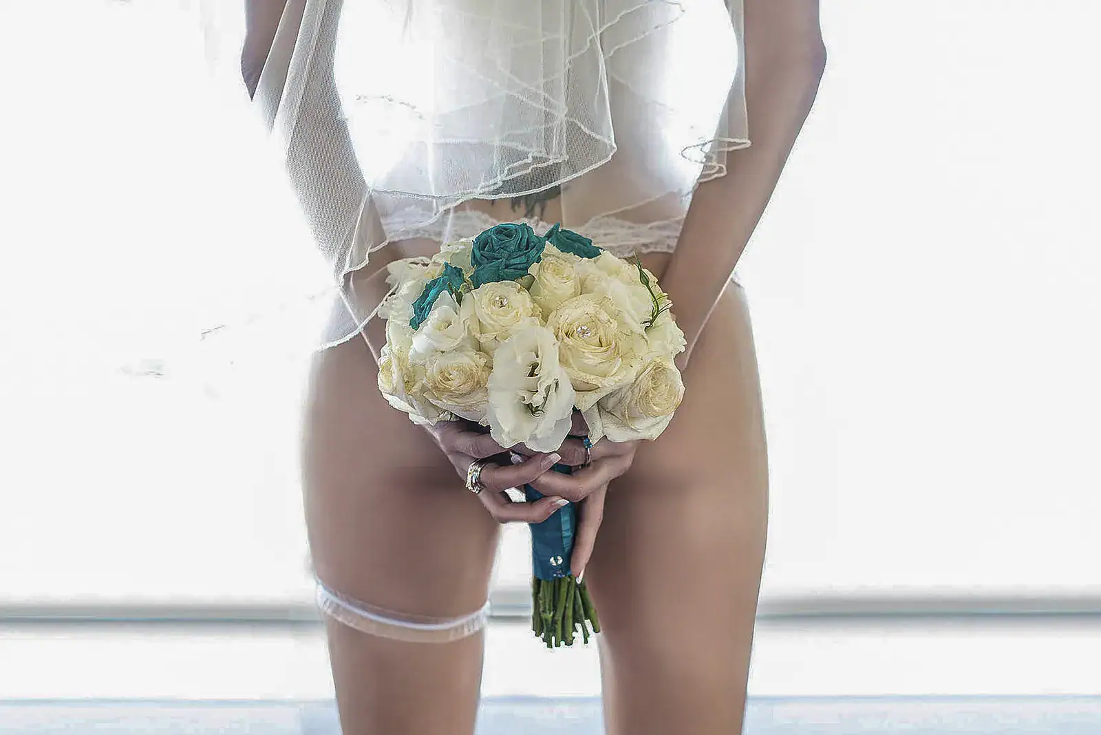 A Bridal Bouquet With a Difference Bride holding her wedding bouquet behind her while wearing white bridal lingerie during a boudoir shoot